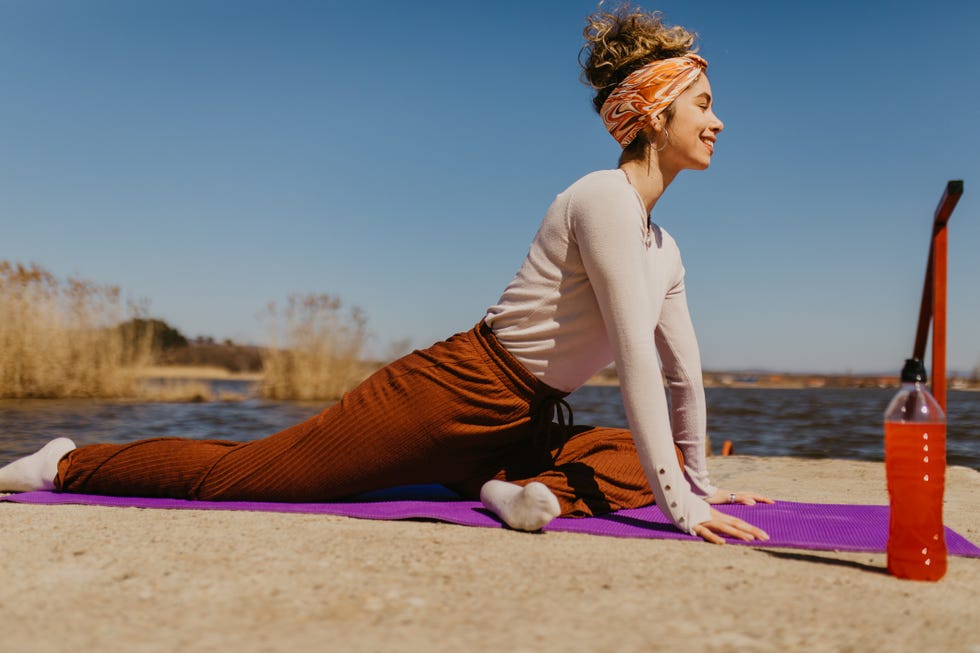 young woman enjoying doing yoga on a sunny day by the lake