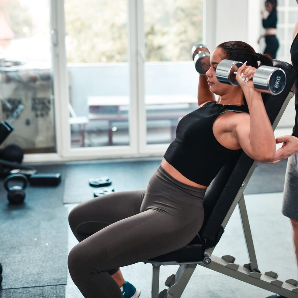 female athlete impressing fitness instructor with shoulder press dumbbell exercise
