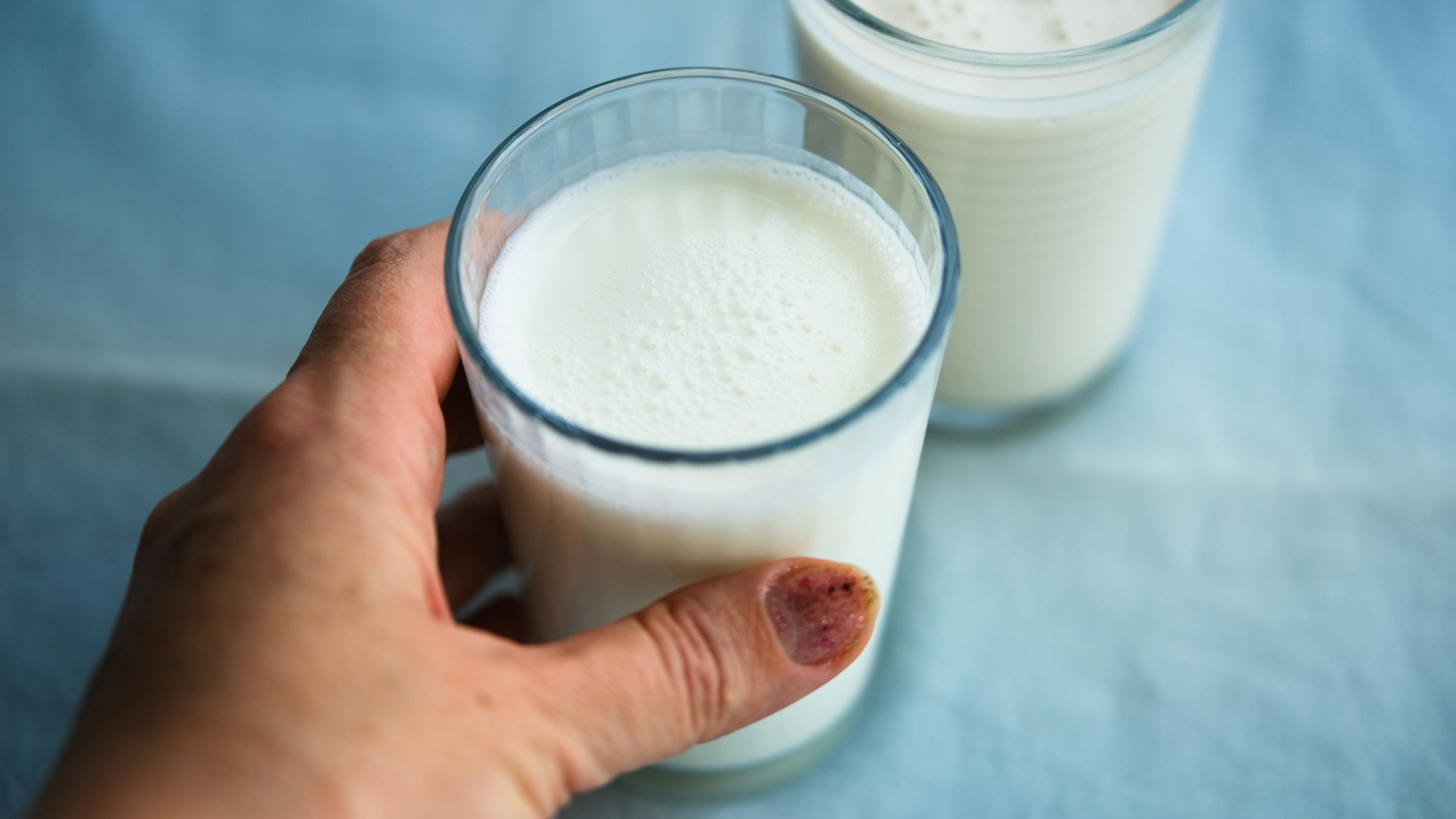 Hand holding one glass of kefir, a white liquid, with another glass of kefir behind it