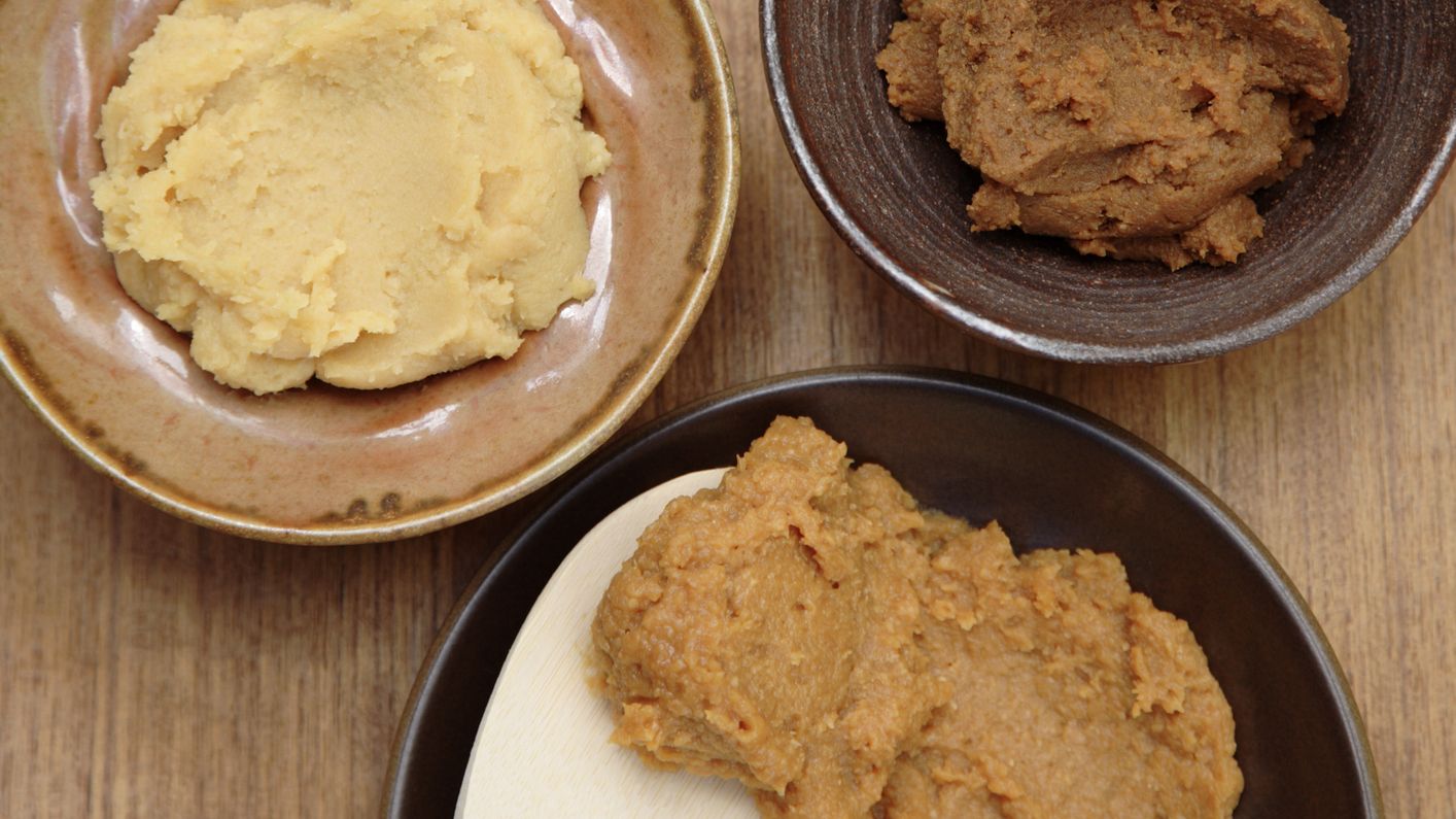 Selection of three different-colored miso pastes in small bowls, a wooden spoon is in one bowl