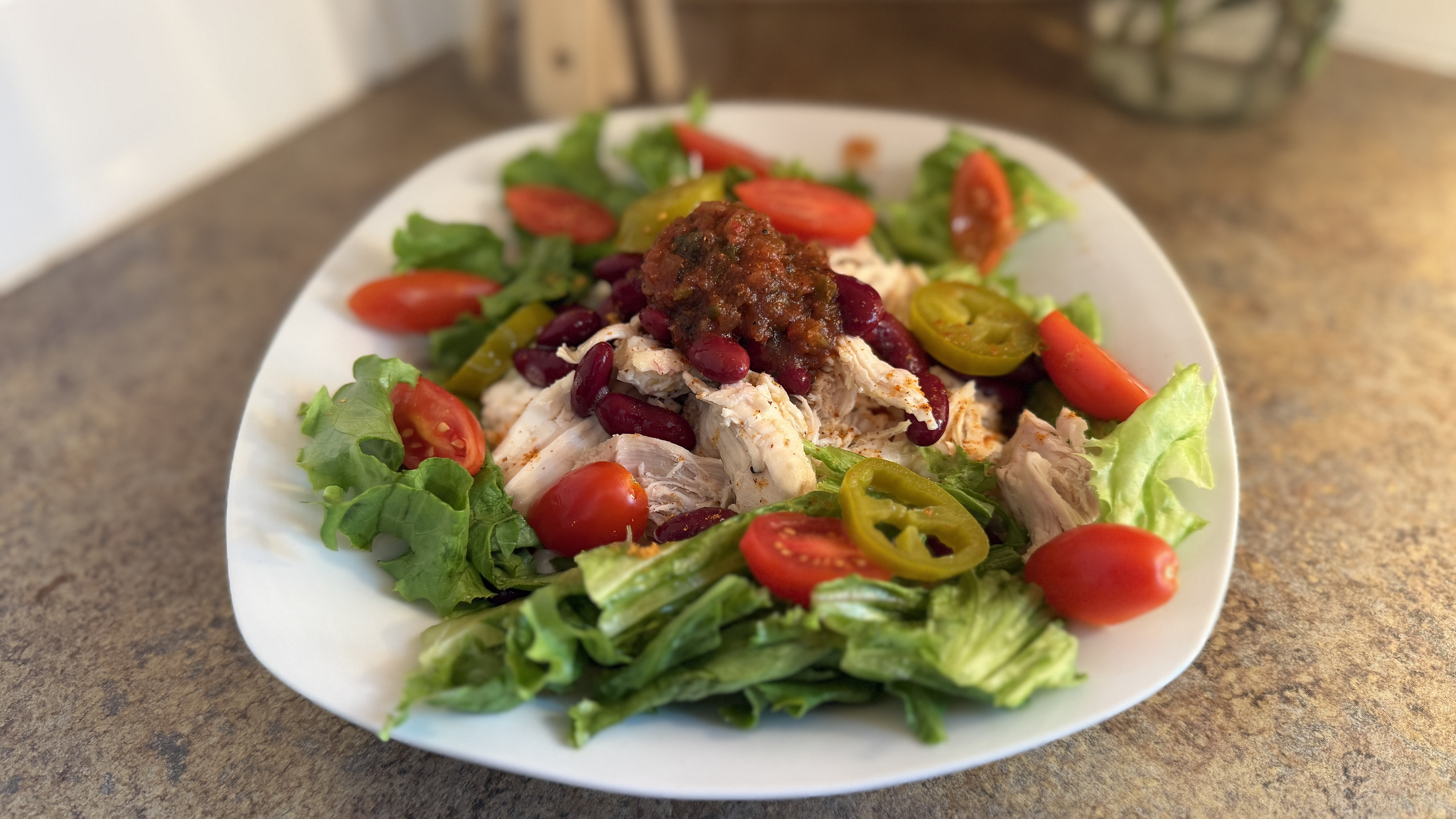 Plate of salad, with bed of lettuce topped with ingredients including cherry tomatoes, chicken, and jalape&amp;ntilde;os