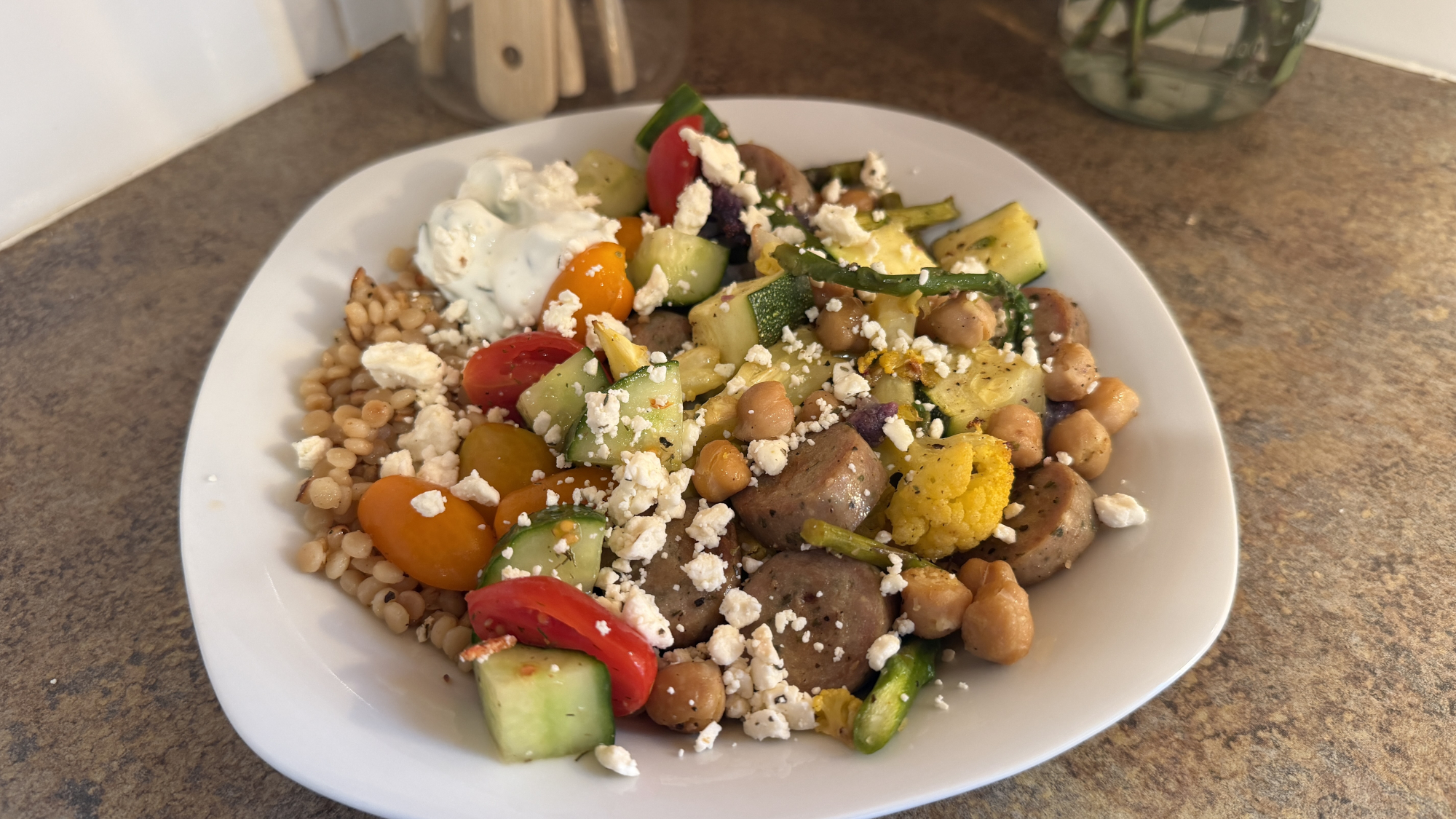 Plate of salad, including sausage slices, cucumber, tomato, feta cheese and cous cous