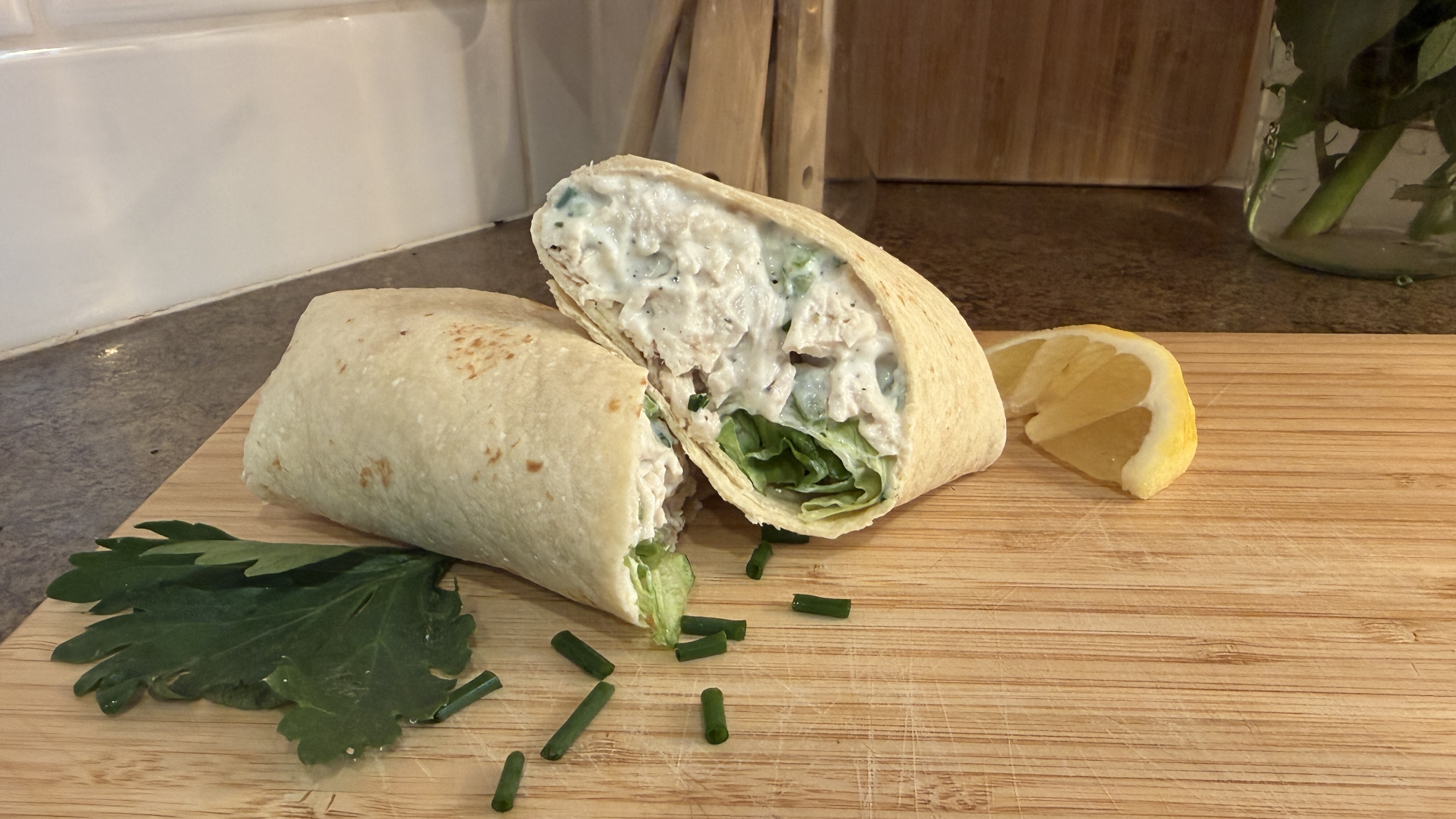 A wrap cut in half showing filling chicken salad filling on wooden chopping board
