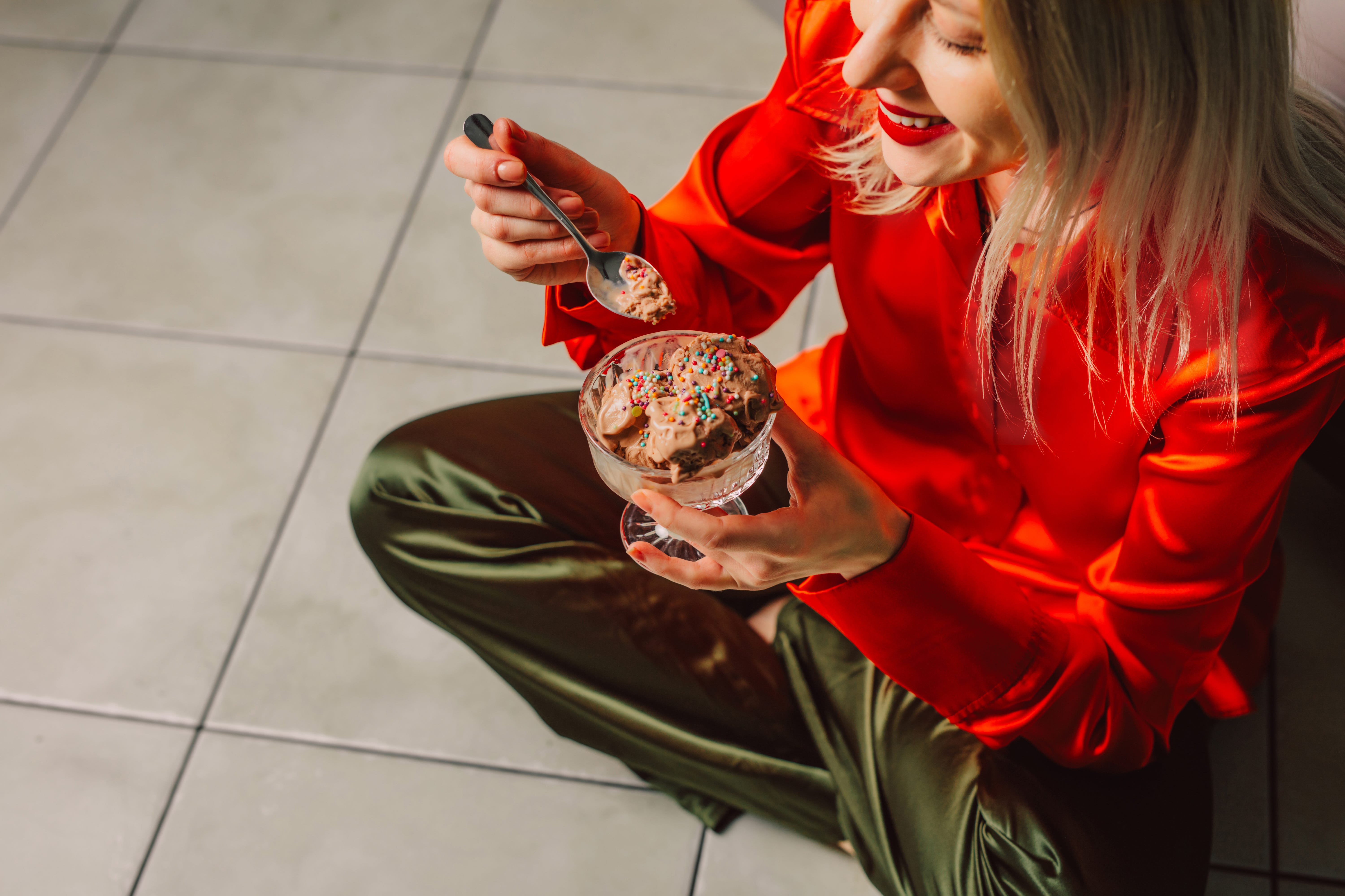 Woman with blonde hair eating ice cream on kitchen floor in stylish attire Woman with blonde hair eating ice cream on kitchen floor in stylish attire