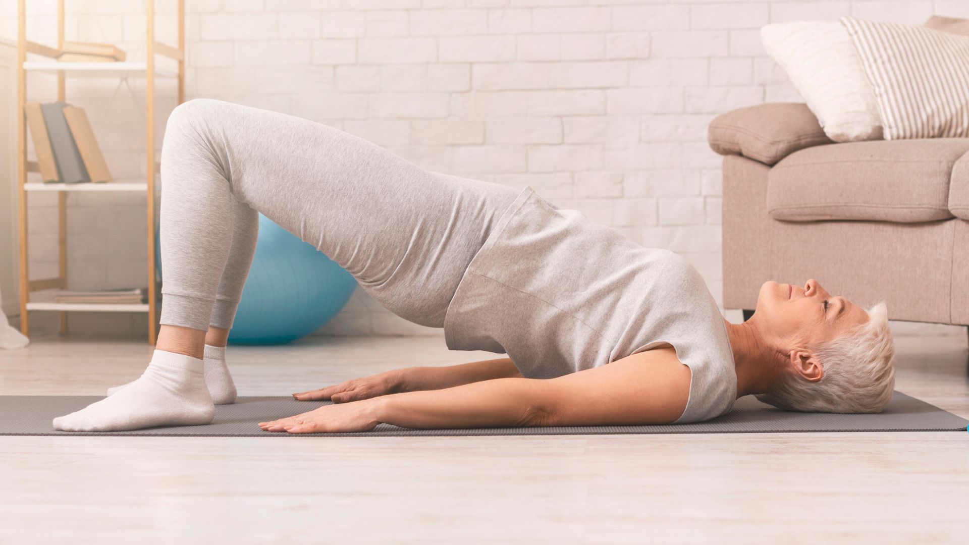 Une femme âgée effectue l’exercice du pont sur un tapis de yoga.