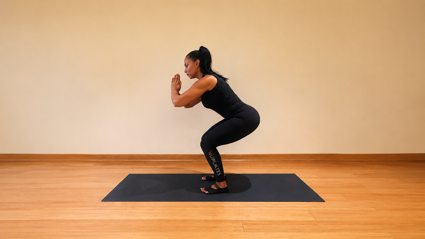 Nicolle Lopez-Lamberty performs a squat, with her knees and hips bent, hands clasped in front of chest.