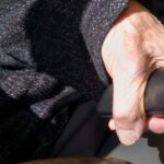 A close-up of an elderly woman's hand clutching her glasses case ti…