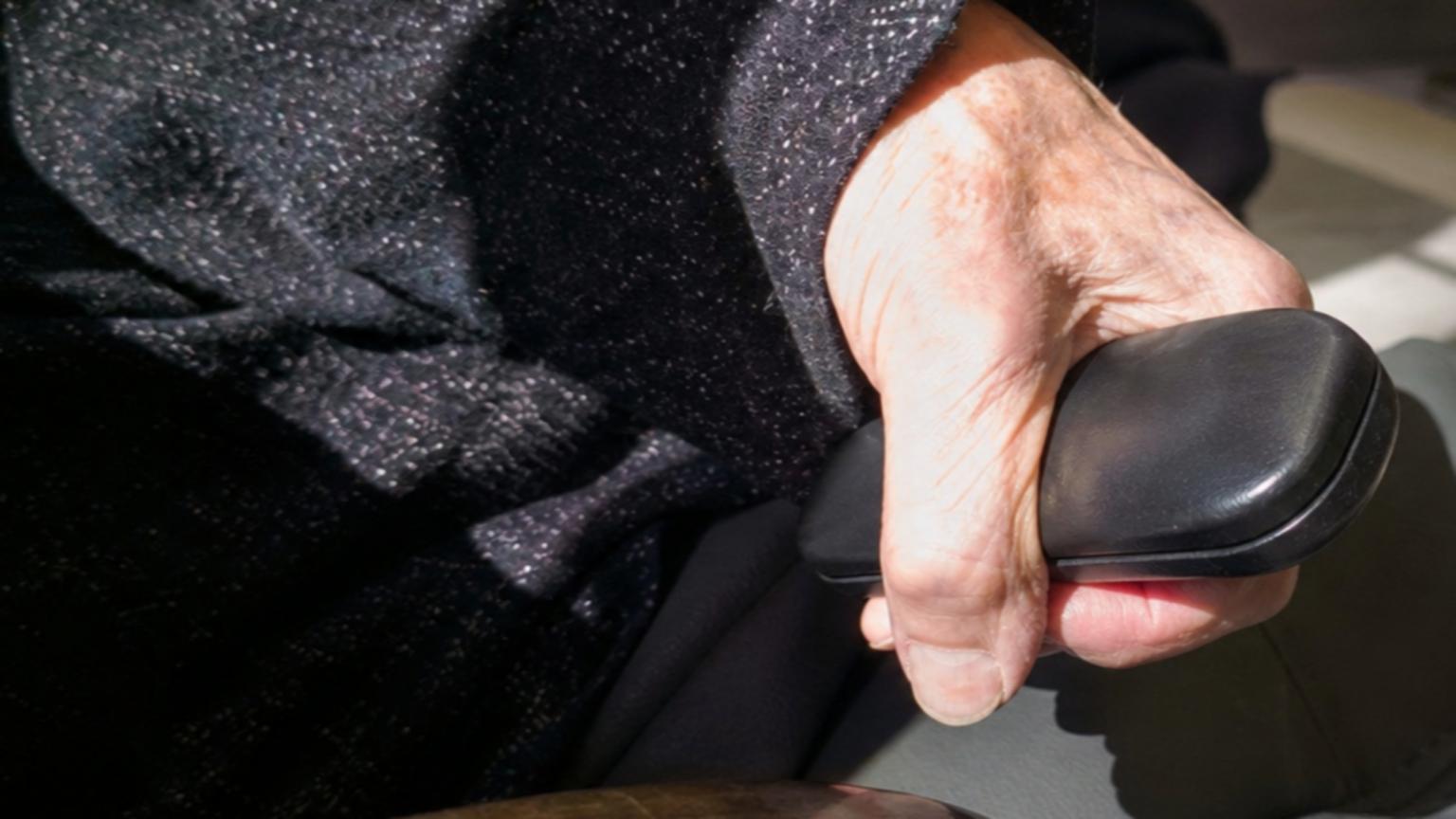 A close-up of an elderly woman's hand clutching her glasses case ti…