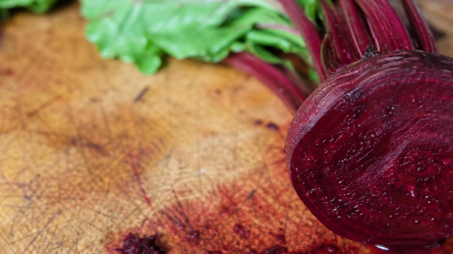 A vibrant, freshly cut beetroot lies on a rustic wooden cutting boa…