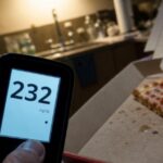 A dimly lit kitchen at night, with a pizza box open on a counter. B…