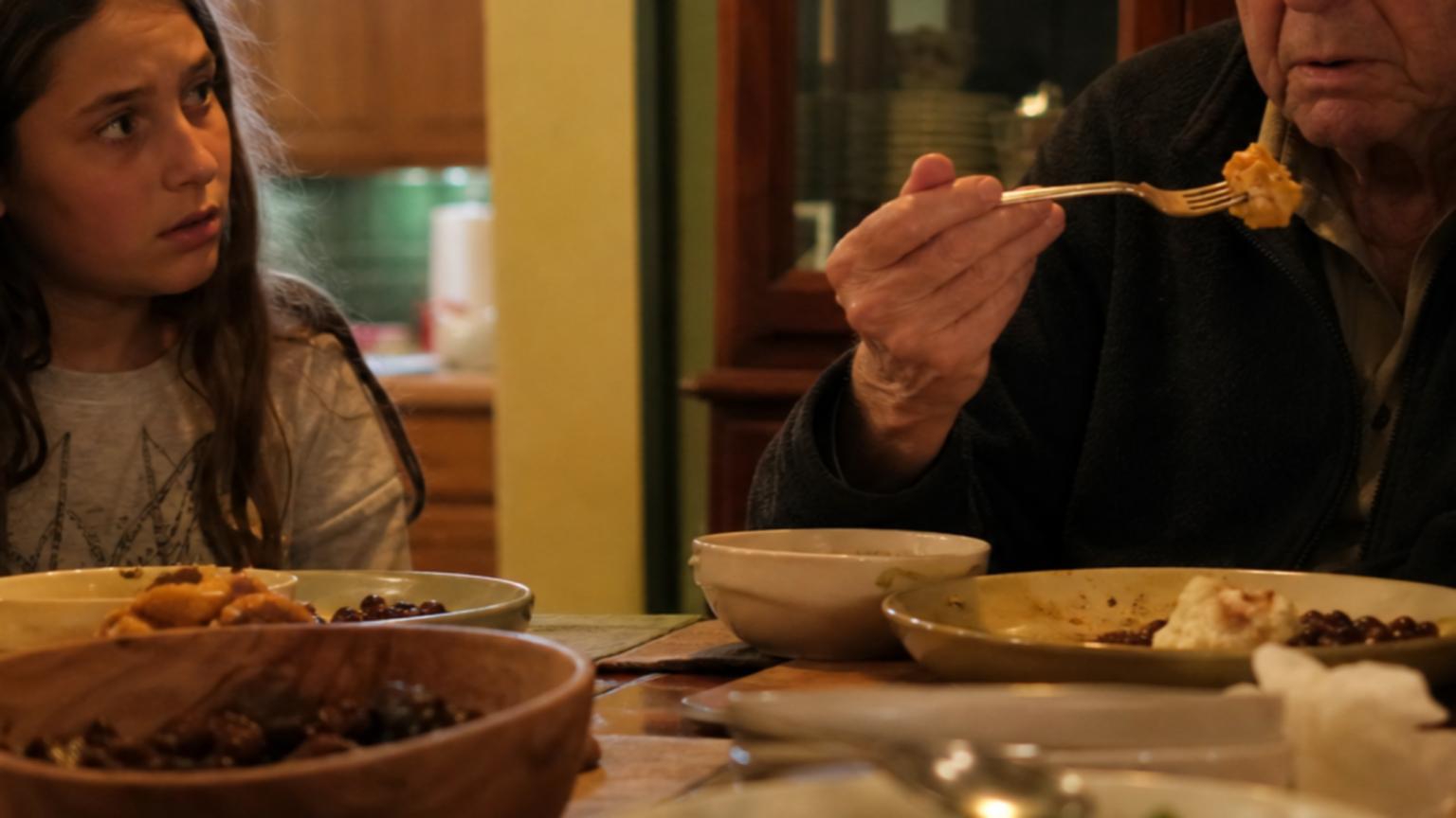 In the soft afternoon light of a cozy dining room, a 71-year-old ma…